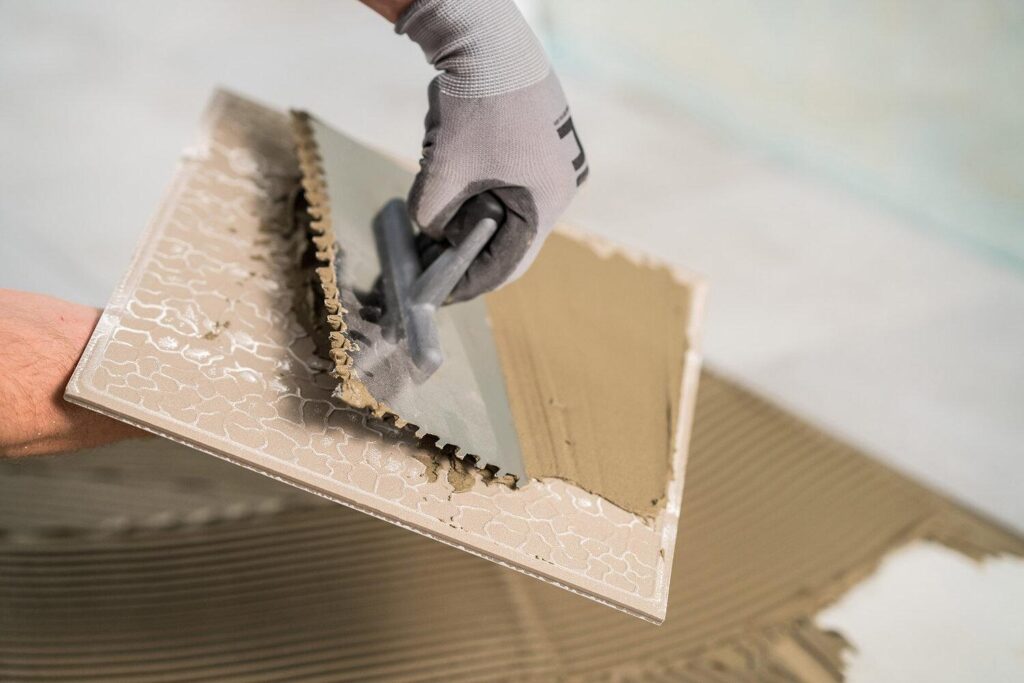 Close up of a tiler back buttering a tile lengthways.