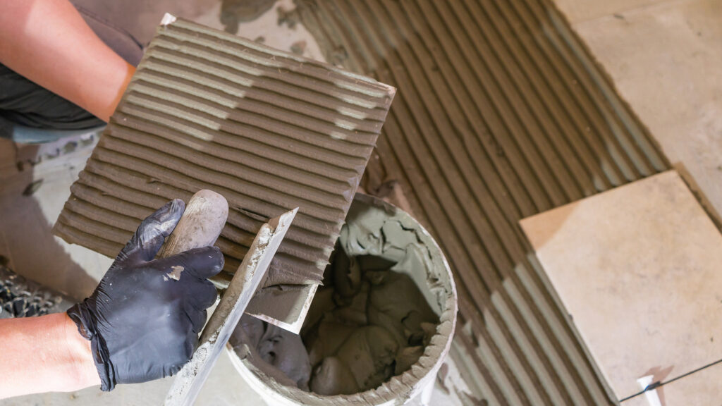 Close up of a tiler back buttering a tile lengthways.