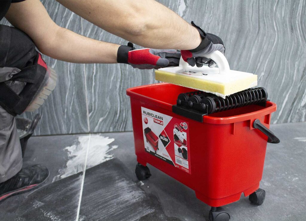 Met de RUBI Triple SuperPro Washboy en een sponsspaan wordt een tegelvloer schoongemaakt. 